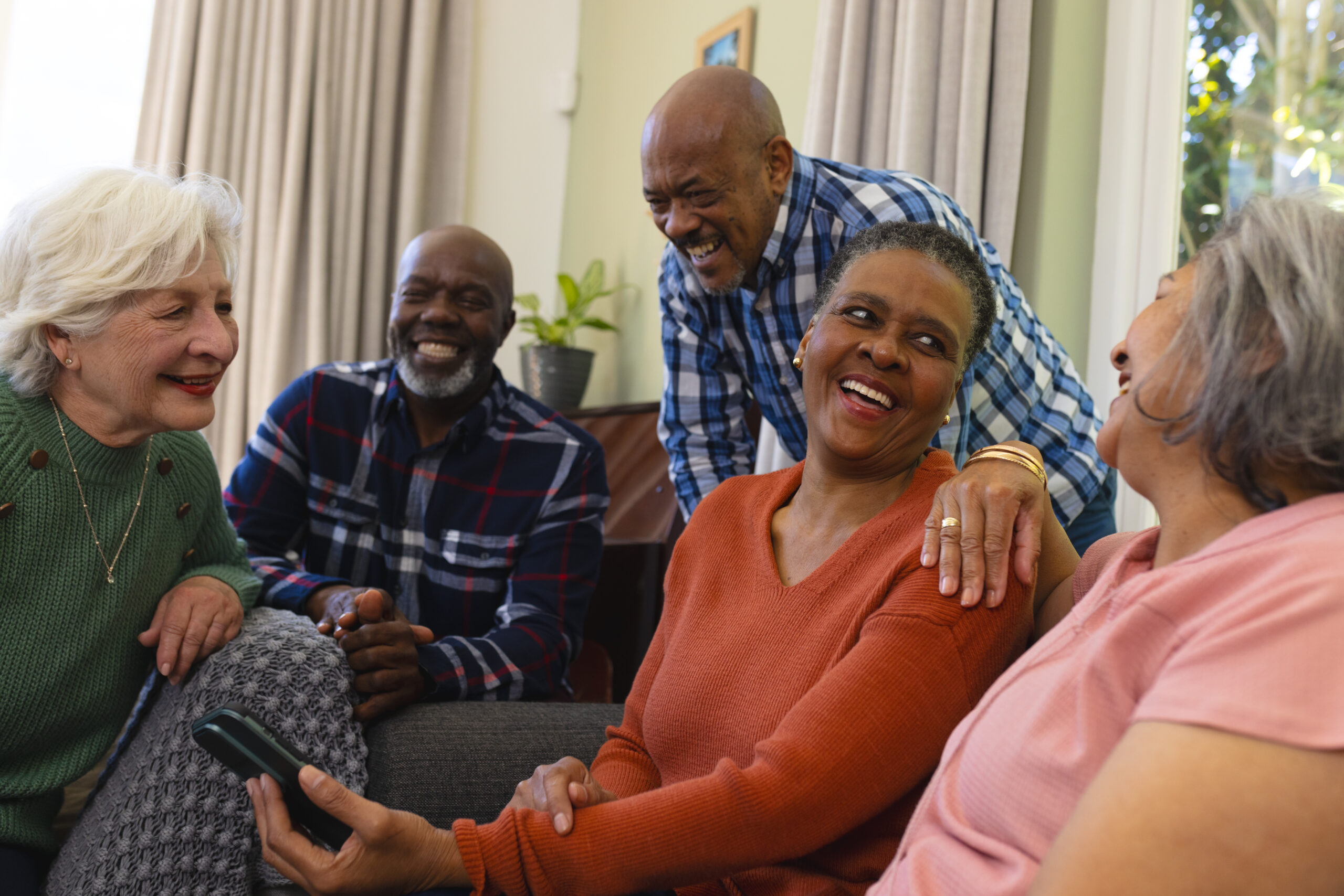 Happy diverse group of senior friends having video call and discussing in sunny living room. Retirement, friendship, domestic life and senior lifestyle, communication, technology, unaltered.
